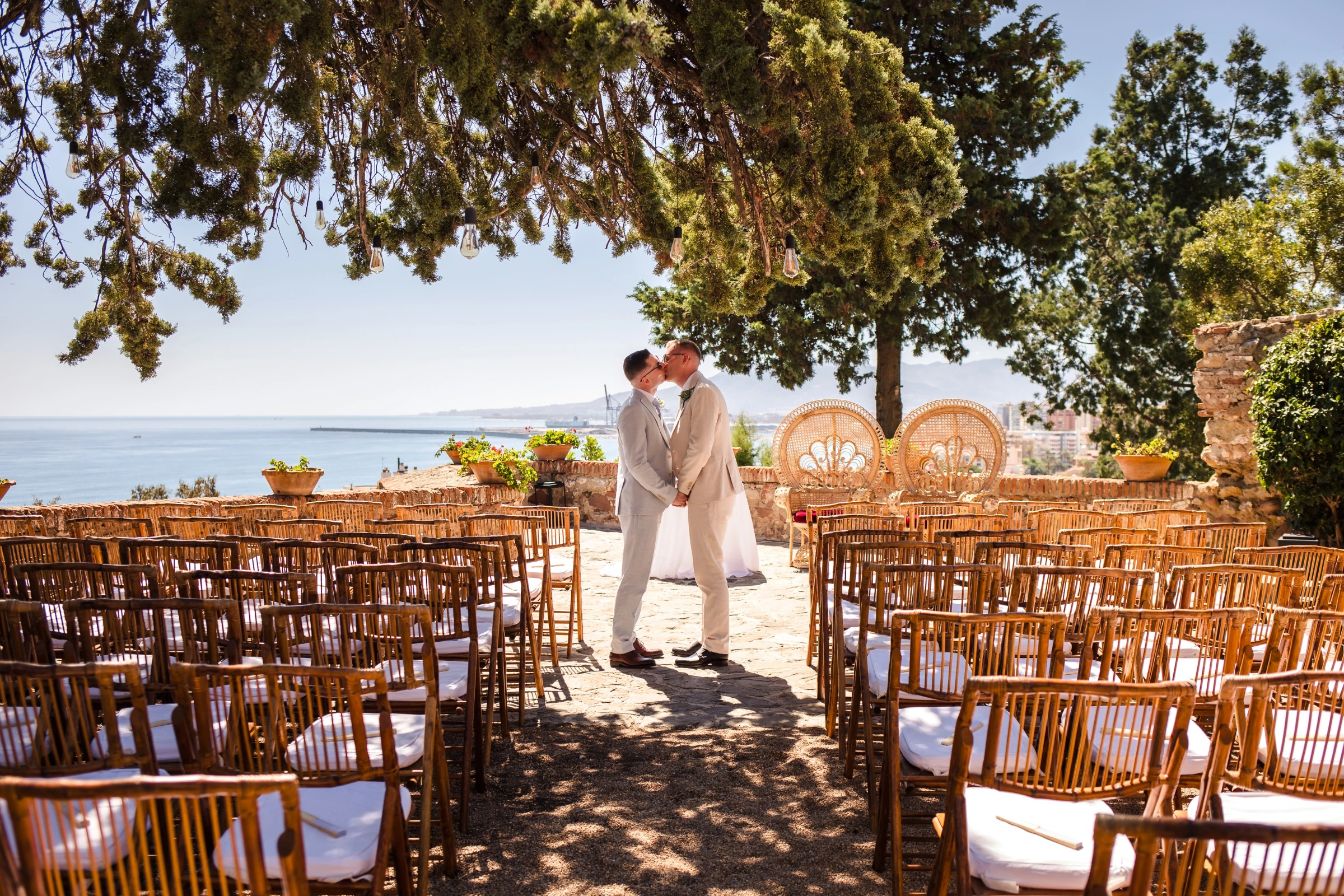Bride and groom kissing under tree shade at outdoor ceremony site, guests seated in rows. — Wedding at Hotel Only You, Malaga, spain