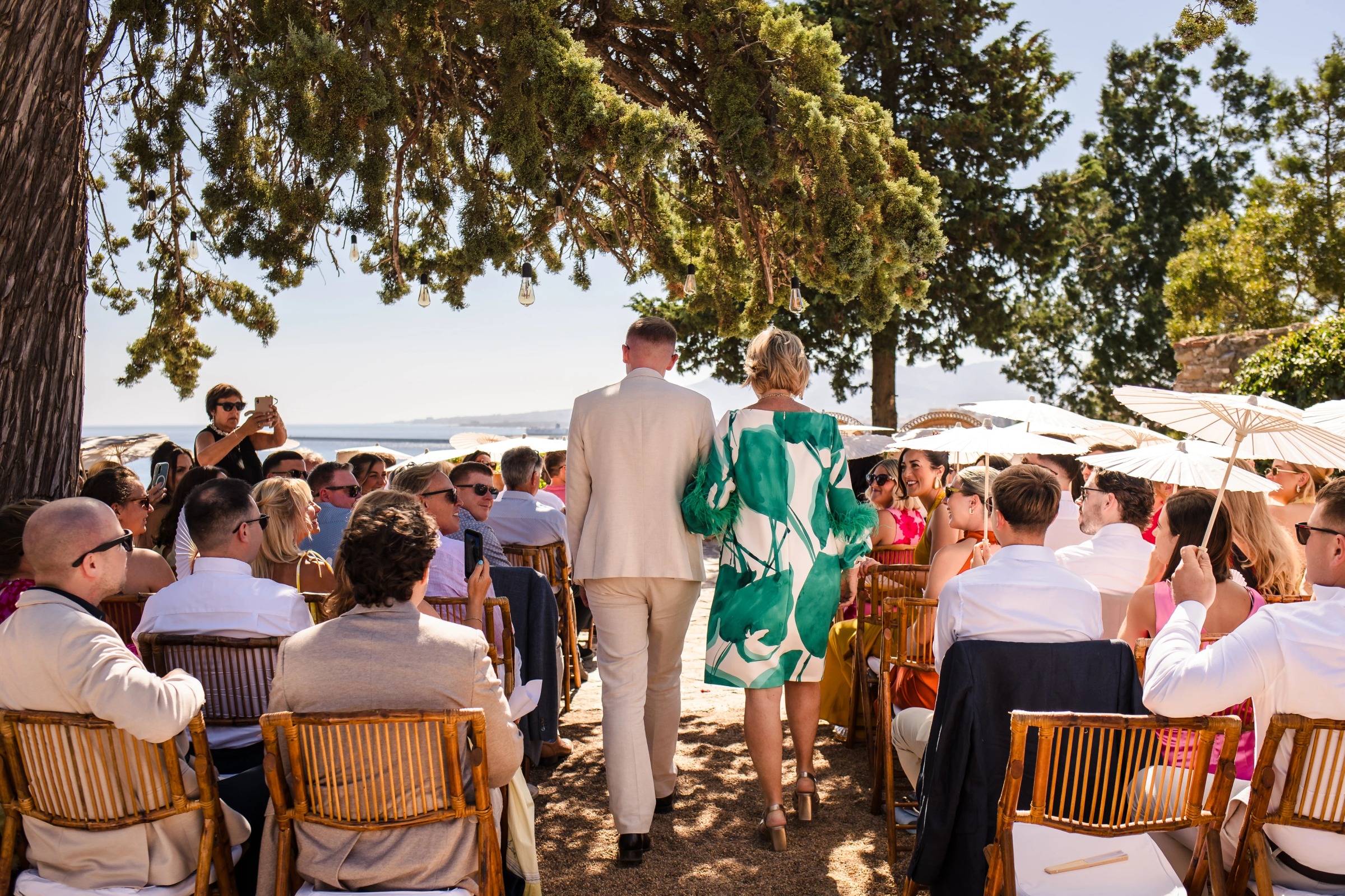 Guests seated in rows watching a ceremony unfold beneath shade trees, with the bride and groom walking down the aisle. — Wedding at Hotel Only You, Malaga, spain
