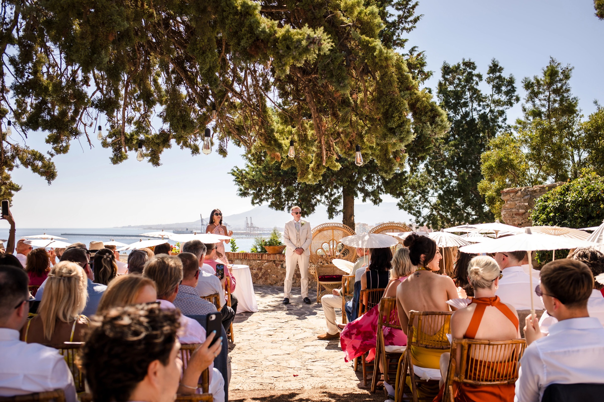 Guests seated on woven chairs watching a ceremony on a sandy beach near water. — Wedding at Hotel Only You, Malaga, spain