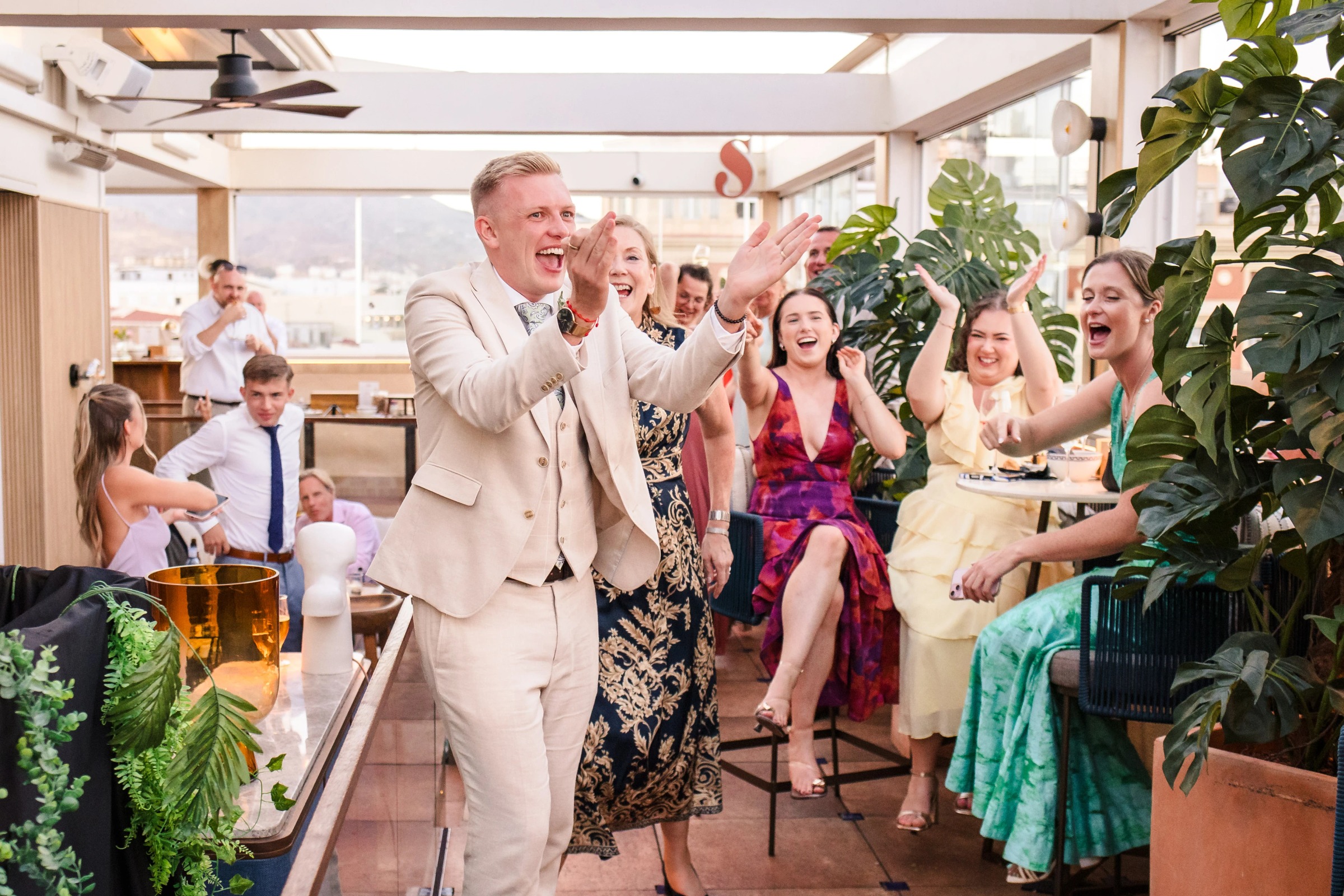 Man in cream suit leading a group in celebratory applause and cheering at an indoor gathering. — Wedding at Hotel Only You, Malaga, spain