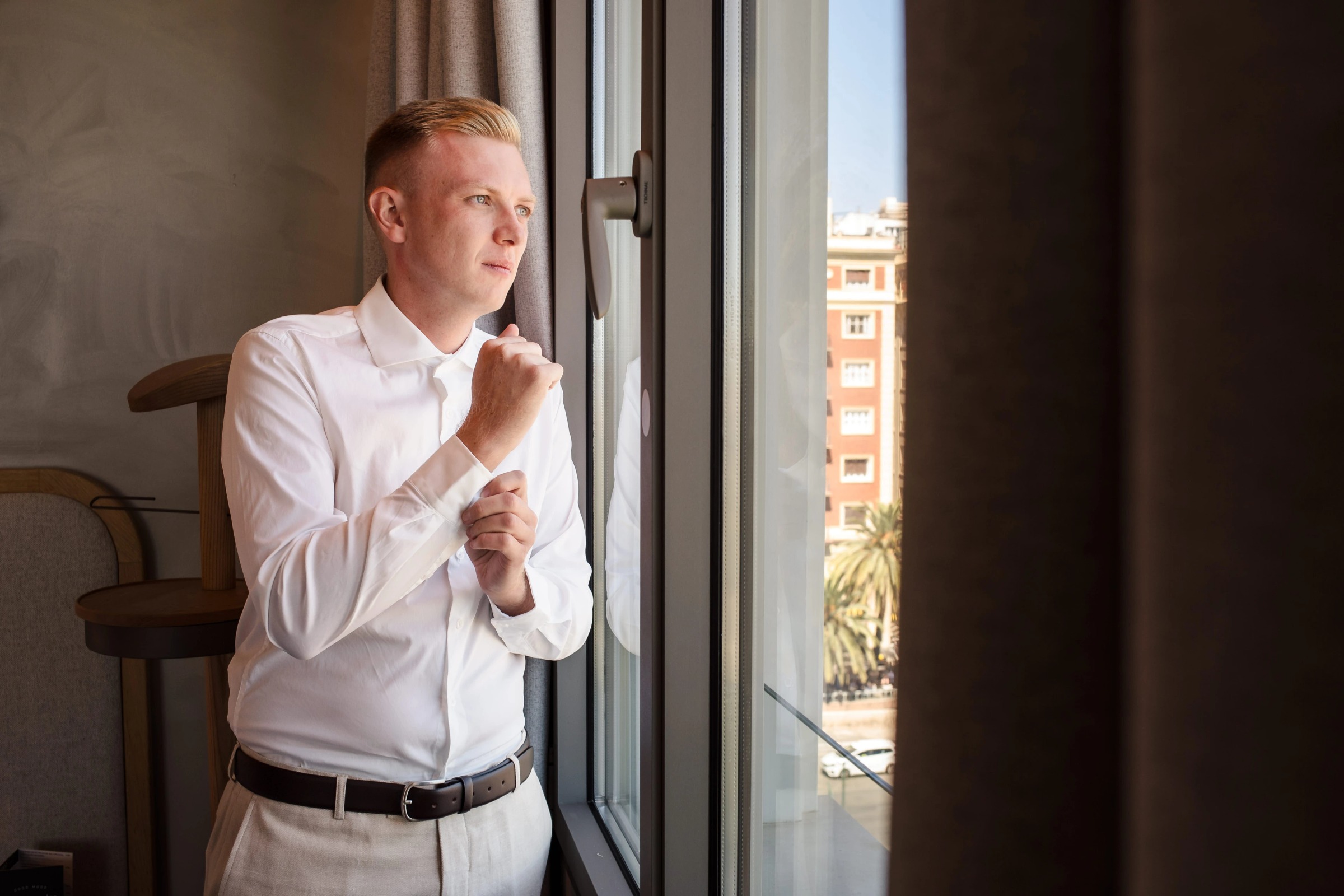 Man in white shirt gazes out a high-rise window, lost in thought. — Wedding at Hotel Only You, Malaga, spain