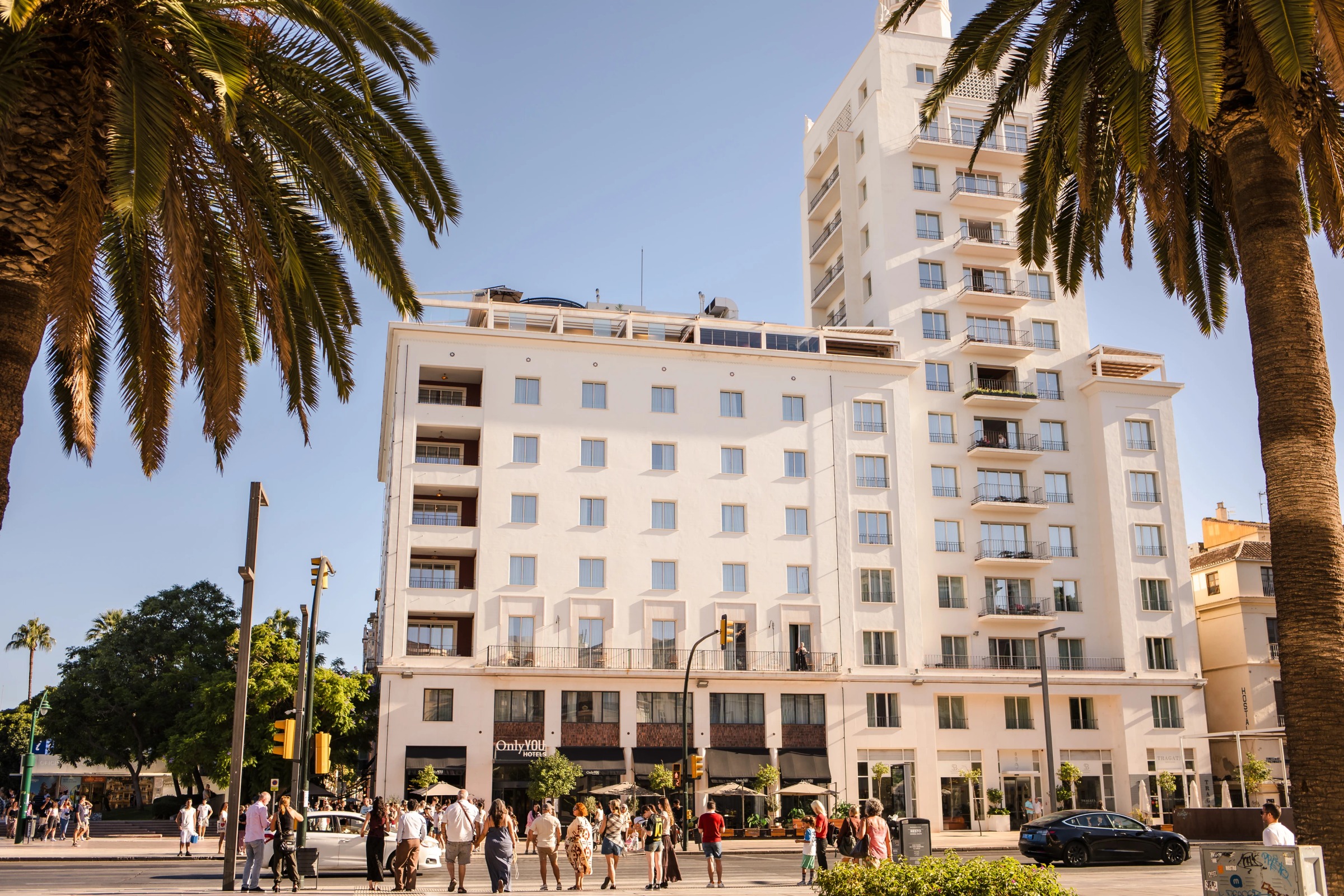 Pedestrians and tourists strolling through a sunlit plaza in front of a residential building. — Wedding at Hotel Only You, Malaga, spain
