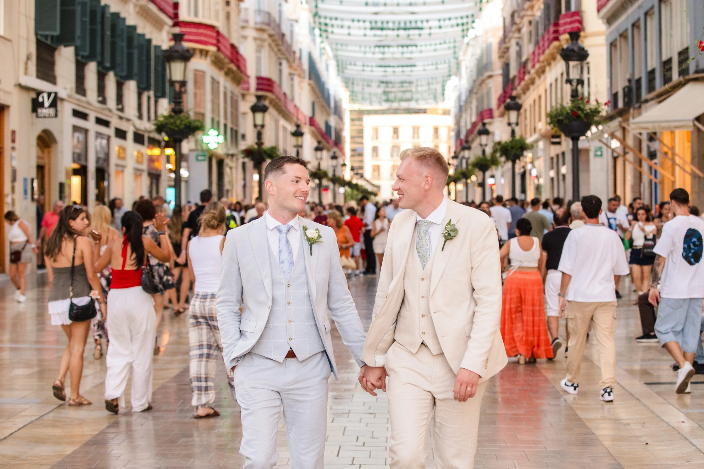 Two grooms walk hand-in-hand down a pedestrian shopping street, smiling at each other. — Wedding at Hotel Only You, Malaga, spain