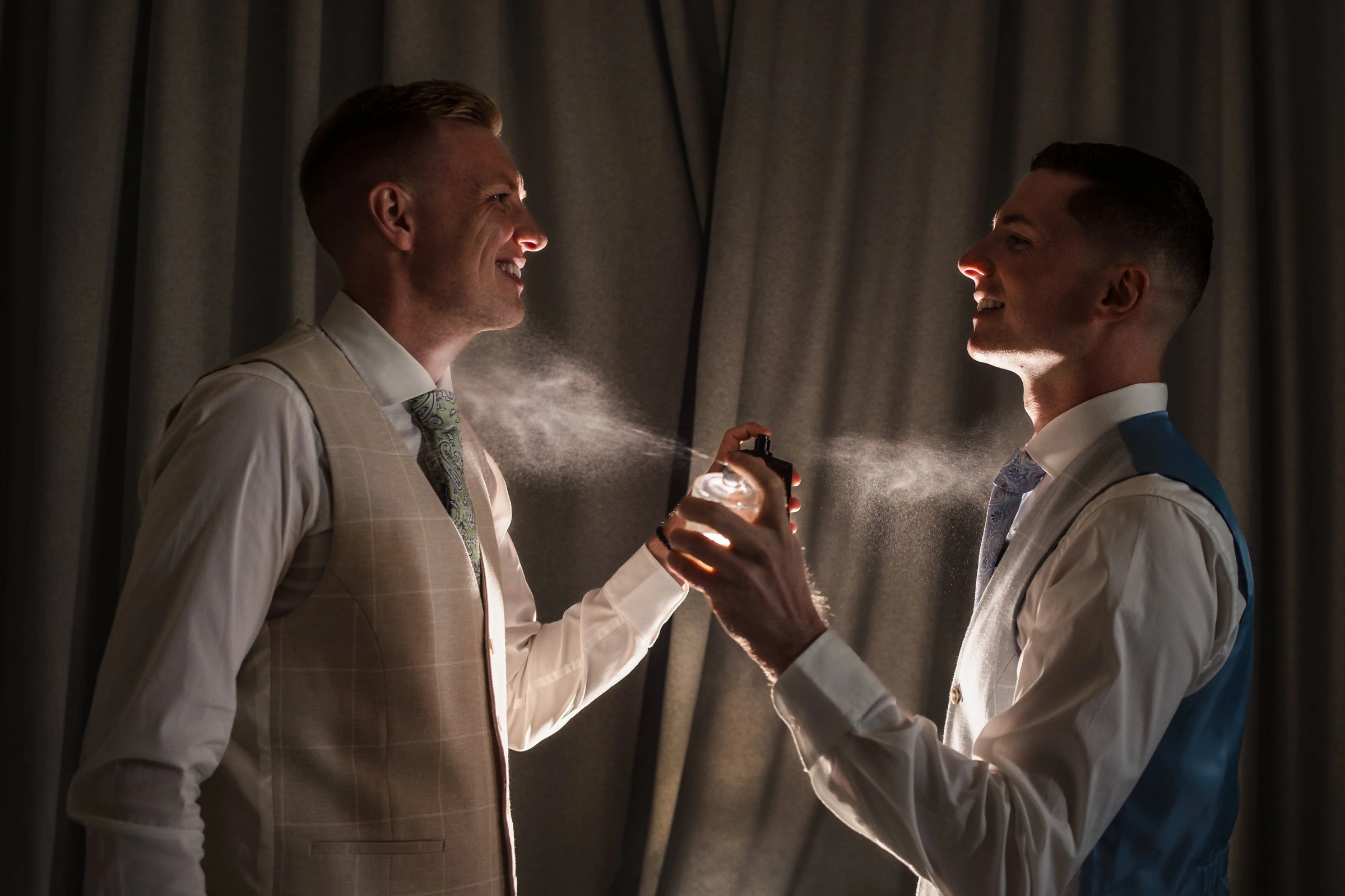 Two men in dress shirts spray cologne or fragrance at each other, laughing and playfully interacting. — Wedding at Hotel Only You, Malaga, spain