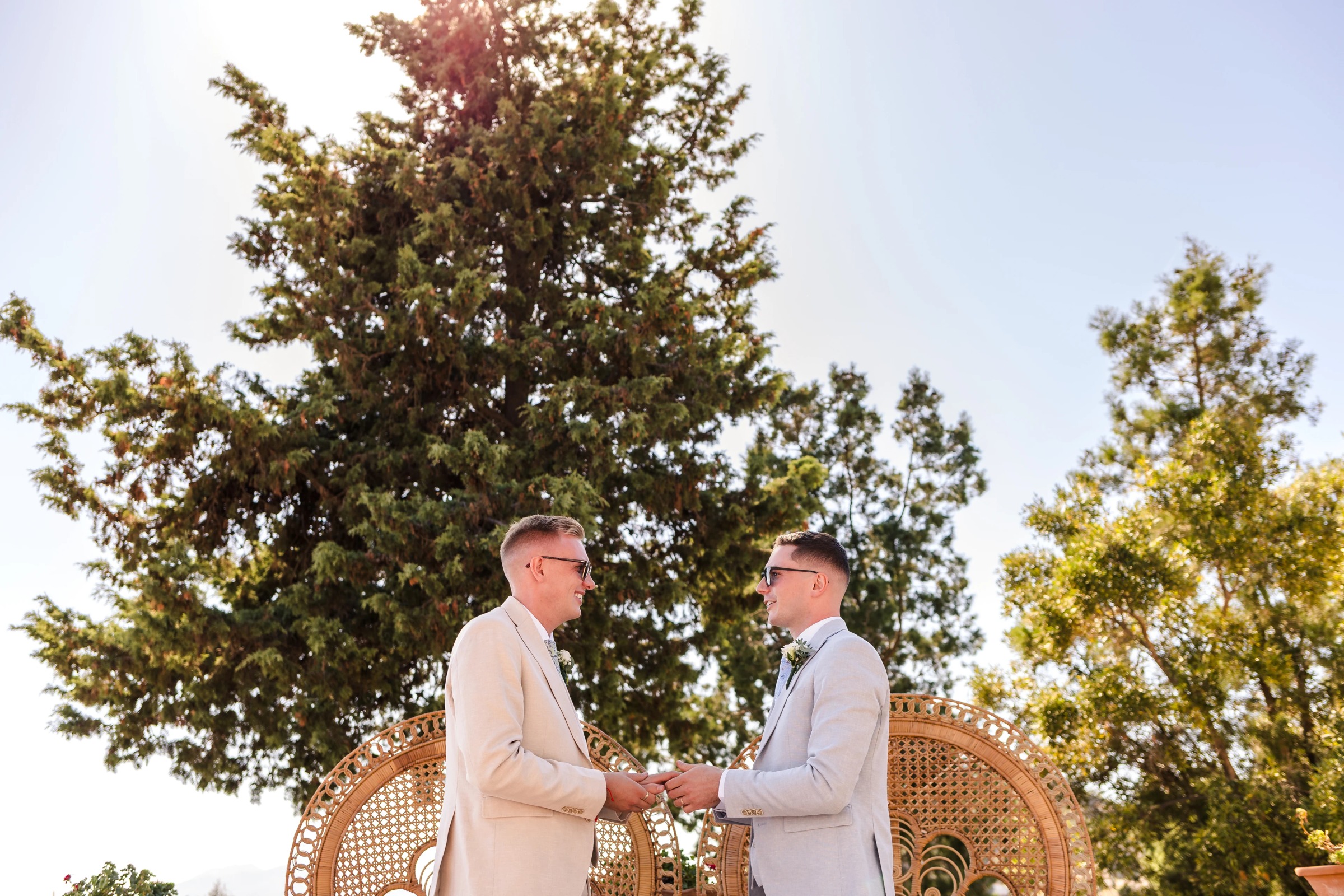 Two men in light suits shake hands and converse outdoors, standing before large trees. — Wedding at Hotel Only You, Malaga, spain