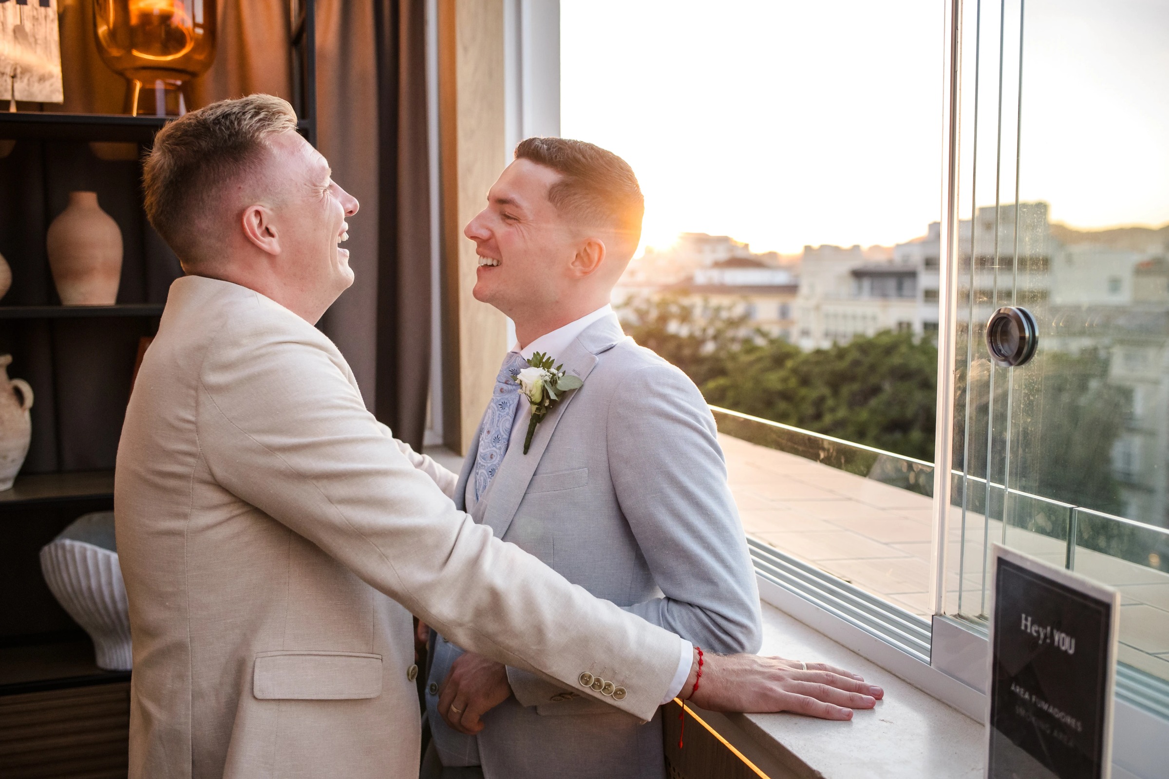 Two men in suits embrace and smile at each other on a high-rise balcony at golden hour. — Wedding at Hotel Only You, Malaga, spain