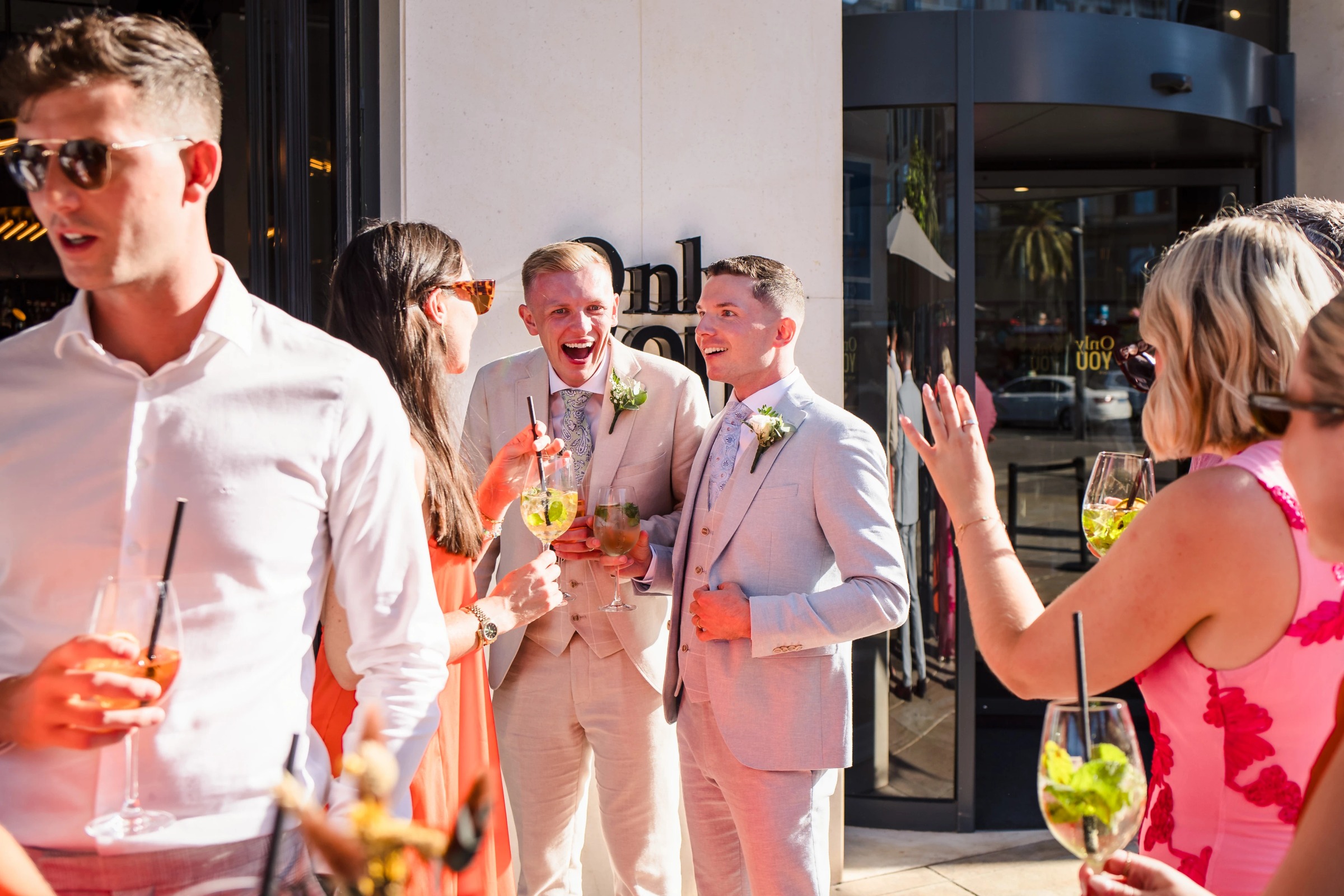 Wedding guests mingling and toasting outdoors in bright sunlight, holding cocktails and champagne flutes. — Wedding at Hotel Only You, Malaga, spain